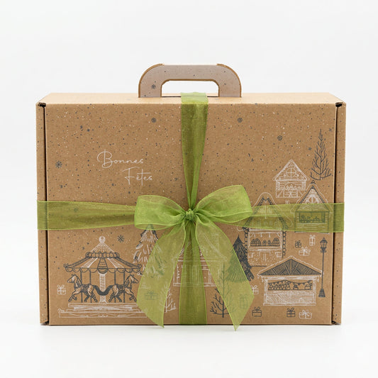 Coffret cadeau de Noël en carton kraft, décoré d’un village festif et fermé par un ruban vert.
