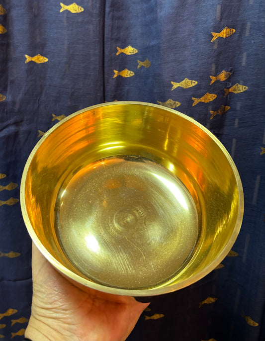  Intérieur d’un bol chantant doré tenu dans une main, devant un tissu bleu à motifs de poissons.